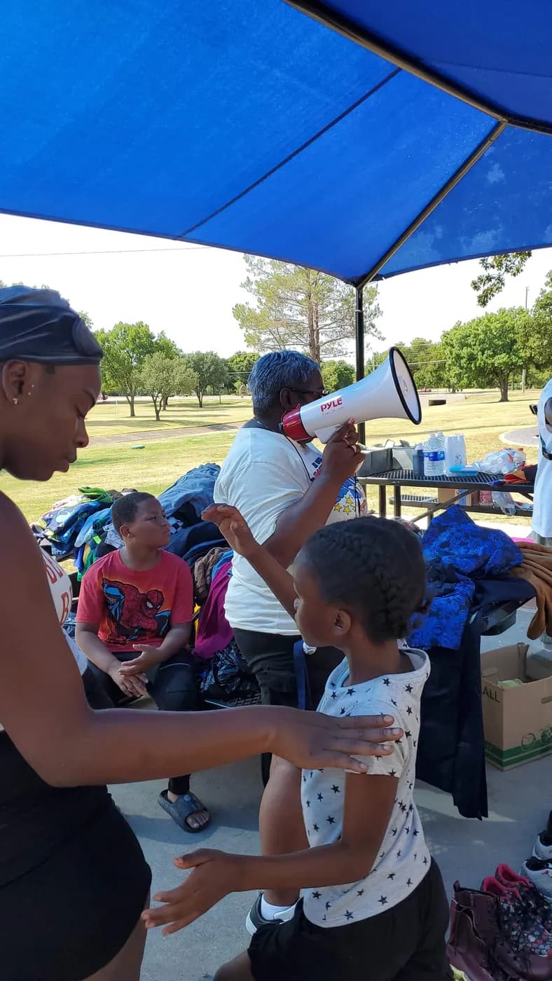 A volunteer with a megaphone welcomes children at a park outreach